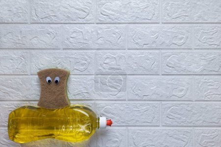 Photo for Funny composition and homework clean up. Top view. Copy space. Fun cleaning. Kitchen sponge with eyes sits on detergent on white brick wall background. Flat lay. Template for advertisement, billboard. - Royalty Free Image