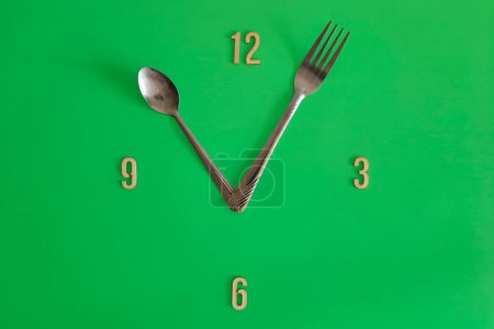 Photo for 11 o'clock. Watch face with the concept of healthy eating, daily regime, diet, meal schedule. Copy space.  Unusual green clock face with with spoon and fork hour hands. Flat lay. Lunch time. - Royalty Free Image