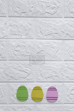 Photo for Simple Easter Decorations. Copy space. Top view. Happy Easter concept. Three Easter eggs cut out of craft cardboard on background of white wall. Flat lay. Place for text. Vertical template. - Royalty Free Image