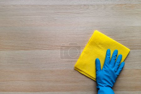 Photo for Scrub-a-Dub. Copy space. Top view. Concept of daily cleaning, washing, housework. Hand in blue rubber glove gets down to business, scrubbing wooden table with yellow rag. Flat lay. Place for text. - Royalty Free Image