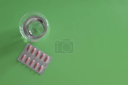 Photo for Tablets and glass of water. Flat lay. Place for text.  Pills in package and water on green background. Vitamins and medicines. Concept of health, treatment, disease prevention. Copy space. Top view. - Royalty Free Image
