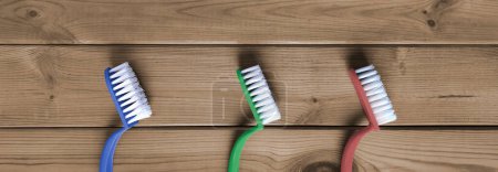 Photo for Banner with plastic cleaning brushes. Flat lay.  Three multi-colored kitchen scrub-brushes in row on background of wooden tabletop. Top view. Header for website, blog, article, cover. - Royalty Free Image