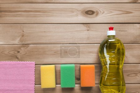 Photo for Dishwashing set. Copy space. Top view. Kitchen cleaning sponges, detergent liquid, microfiber cloth on wooden table background with place for text. Routine everyday housework. - Royalty Free Image