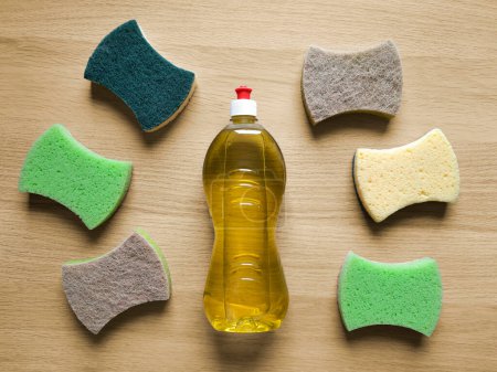 Photo for Background with liquid detergent and kitchen cleaning sponges. Bottle with yellow household chemicals and washcloths for washing dishes on wooden table. Concept housework clean up, clean house. - Royalty Free Image