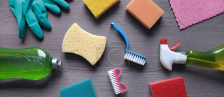 Photo for Cleaning products banner. Top view. Kitchen sponges, cleaning liquid, window spray, synthetic rags, rubber gloves and brushes on wooden table. Header for hardware store, cleaning company, website. - Royalty Free Image