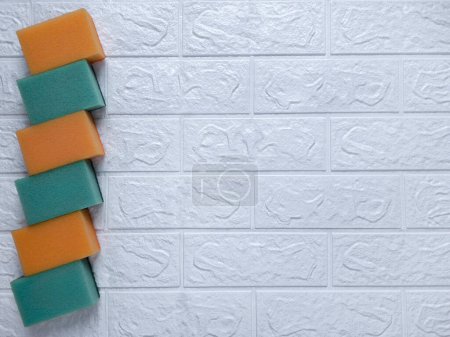 Photo for Set of kitchen sponges for cleaning. Flat lay. Copy space. Green and orange washcloths on white brick wall background. Cleaning Services Concept - house, apartment, office cleaning. Place for text. - Royalty Free Image