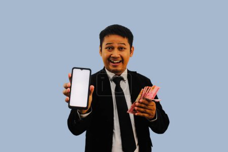 Adult Asian man smiling happy while showing blank mobile phone screen and holding paper money