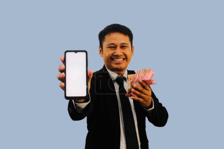 Adult Asian man smiling happy while showing blank mobile phone screen and holding paper money