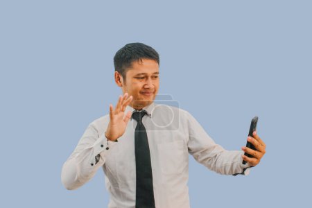 Adult Asian man waving hand with happy face expression during video call