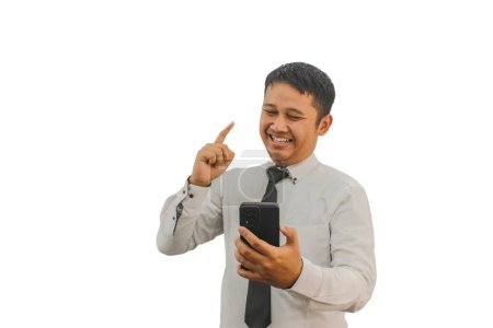 Photo for Adult Asian man smiling and pointing one hand up while holding mobile phone - Royalty Free Image