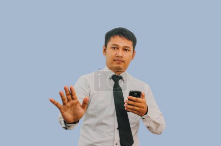 Foto de Adulto asiático hombre mostrando stop hand signo cuando mirando a su teléfono móvil pantalla - Imagen libre de derechos