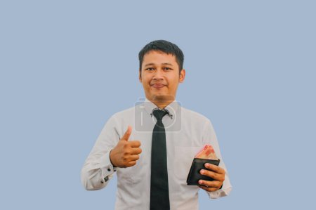 Erwachsener asiatischer Mann lächelt, während er Geldbörse mit Geld in der Hand hält und Daumenfinger zeigt