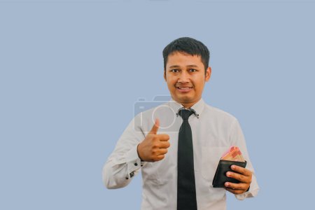 Erwachsener asiatischer Mann lächelt, während er Geldbörse mit Geld in der Hand hält und Daumenfinger zeigt