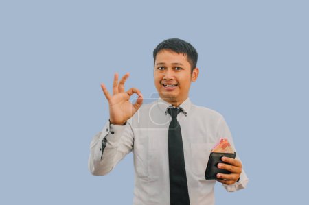 Foto de Adulto asiático hombre sonriendo mientras sostiene la cartera con dinero y dar OK dedo signo - Imagen libre de derechos