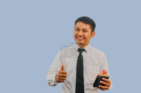 Foto de Adulto asiático hombre sonriendo mientras sostiene la cartera con dinero y dar dedo pulgar signo - Imagen libre de derechos