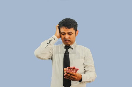 Photo for Adult Asian man doing thinking gesture while holding Indonesia paper money - Royalty Free Image