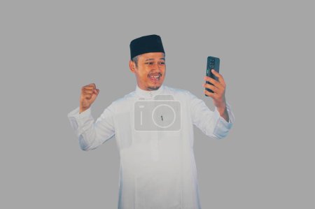 musulmán asiático hombre apretado puño mostrando emoción mientras mira a su teléfono móvil