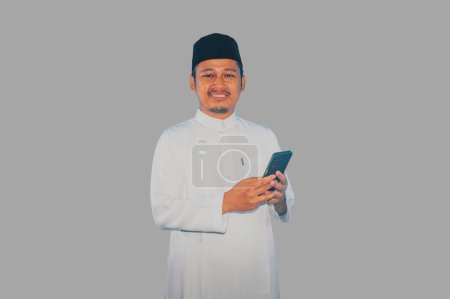 musulmán asiático hombre sonriendo en cámara mientras sostiene su móvil