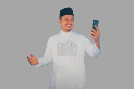 Photo for Moslem Asian man smiling happy while looking to his mobile phone - Royalty Free Image