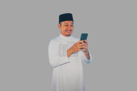 Moslem asiatischer Mann lächelt glücklich, wenn er mit seinem Handy SMS schreibt