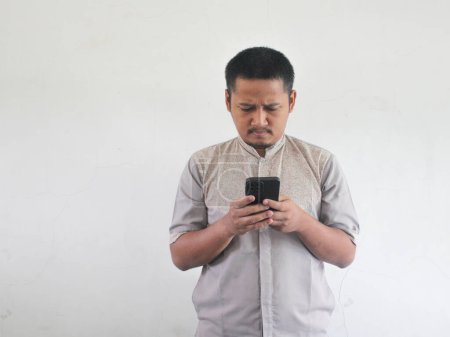 Photo for Adult Asian man seriously think something while typing on his mobile phone - Royalty Free Image