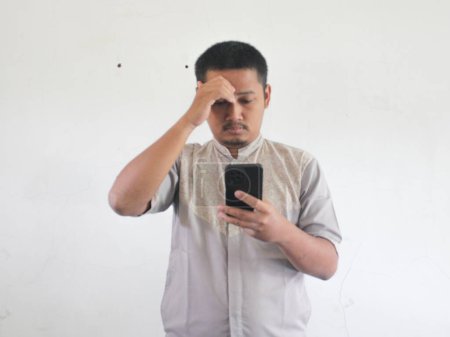 Photo for Asian man holding his mobile phone with sad expression - Royalty Free Image