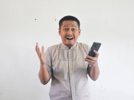 Photo for Adult Asian man looking to his mobile phone with wow expression - Royalty Free Image