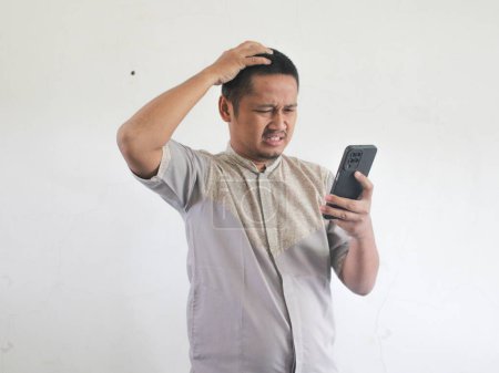 Adult Asian man showing confused expression when looking to his phone