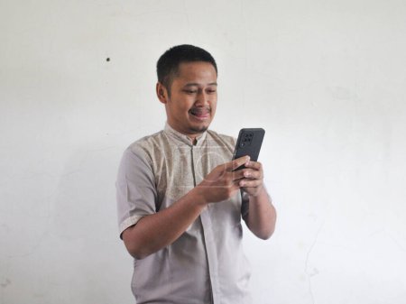 Erwachsener asiatischer Mann hält Handy mit lustigem Gesichtsausdruck