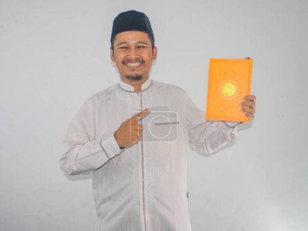 Musulman Asiatique souriant tout en pointant vers un Coran qu'il tient