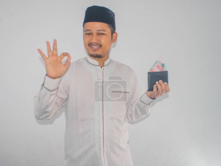 Adult muslim Asian man smiling and give OK finger sign while holding money