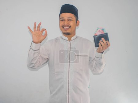 Adult muslim Asian man smiling and give OK finger sign while holding money