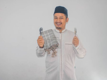 Moslem Asian man smiling happy with hand holding dinning spoon and fork