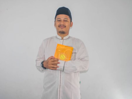 Moslem Asian man smiling at the camera while holding a Al-Qur'an
