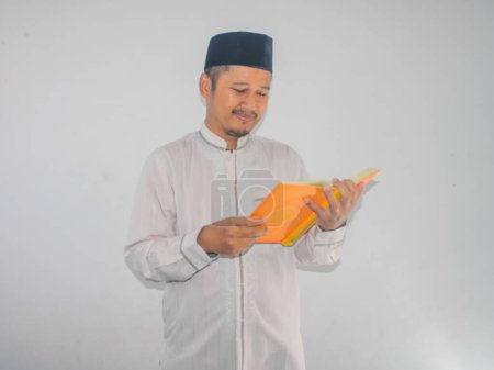Der muslimische Asiate lächelt den Al-Koran an und hält einen Al-Koran in der Hand