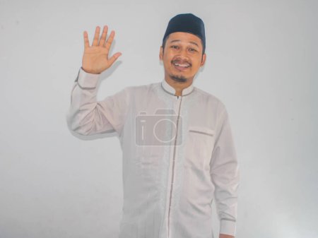 Moslem Asian man showing happy expression when waving hand to greet someone