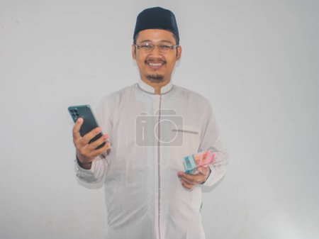 Moslem Asian man smiling happy while holding mobile phone and money