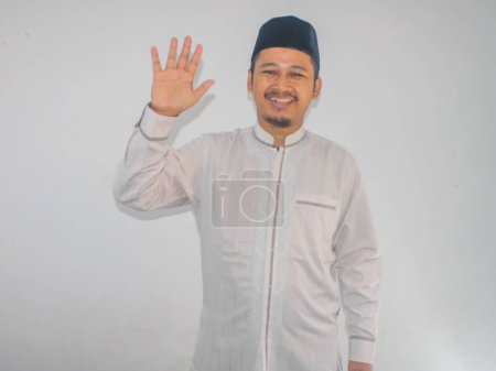 Moslem Asian man showing happy expression when waving hand to greet someone