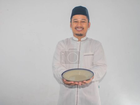 musulmán asiático hombre sonriendo feliz mientras sosteniendo vacío plato de cena