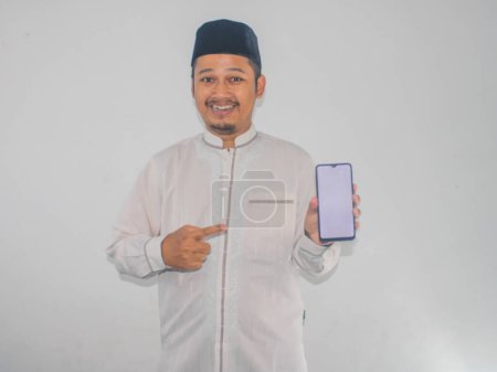 Moslem Asian man smiling and pointing to blank mobile phone screen that he hold
