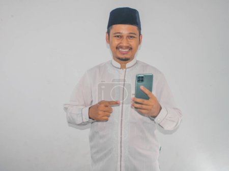 Moslem Asian man smiling and pointing to mobile phone that he hold