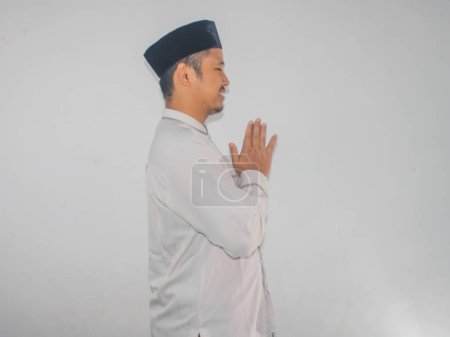 Téléchargez les photos : Vue latérale de l'homme asiatique musulman souriant tout en saluant quelqu'un pendant la célébration du Ramadan - en image libre de droit
