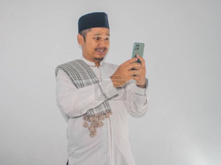 Téléchargez les photos : Musulman asiatique homme sourire heureux lors de l'envoi de SMS à l'aide de son téléphone mobile - en image libre de droit
