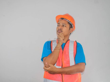 Asiatischer Bauarbeiter mit orangefarbener Weste und Hut sieht man auf der Suche nach Ideen vor weißem Hintergrund