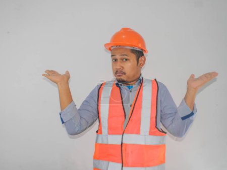 asian worker man wearing orange safety vest uniform and helmet clueless and confused expression with arms and hands raised. Doubt concept.