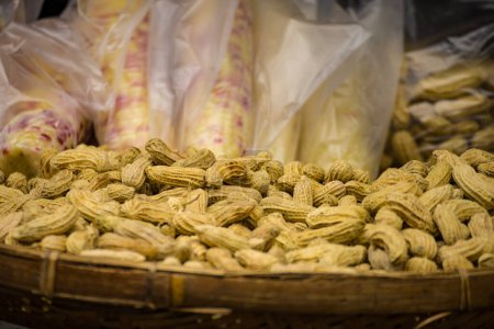 Téléchargez les photos : Un panier d'arachides fraîches bouillies avec un sac de maïs blanc en arrière-plan - en image libre de droit