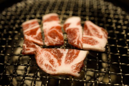  slices of beef being grilled over a charcoal fire