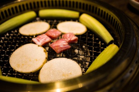  a grill where freshly prepared meat slices and vegetables are being cooked