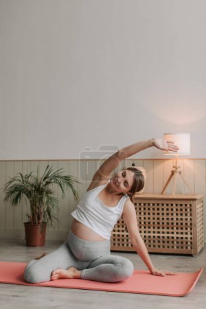 Photo for Top view of happy smiling Pregnant female stretching on mat at home in the morning. Young expectant mother practice stretching yoga. Active flexible woman in sportswear doing exercises. - Royalty Free Image