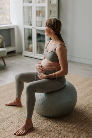 Photo for Pregnant woman in sportswear meditates doing exercises on fitball at home. Respiratory gymnastics before childbirth. Large belly with an unborn baby. Healthy image concept. Fitness for pregnant women - Royalty Free Image